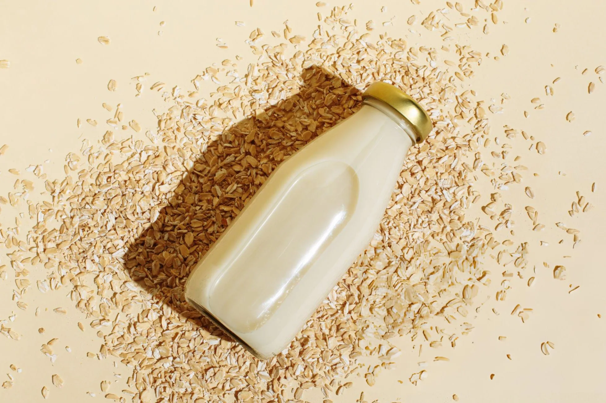 Ranking The 9 Healthiest Oat Milks For A Balanced Diet Healthiest Oat Milks - Oat milk in glass bottle and oatmeal flakes on beige background. Healthy vegan non-dairy organic drink with flakes. Lactose-free milks in minimal flat lay style. Top view